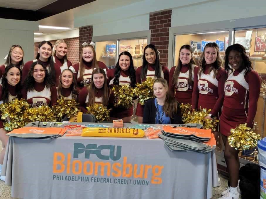 Cheerleaders and PFCU employee at PFCU Bloomsburg table.