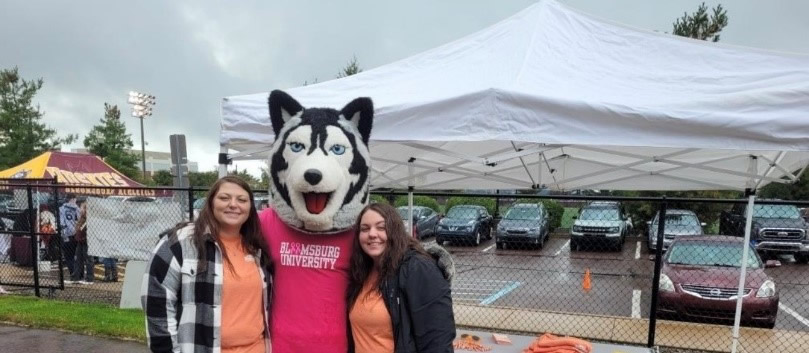 PFCU team members Jocelyn Long (left) and Isabella Crilly (right) posing with Bloomsburg's mascot Roongo at the October 7 game against Kutztown.